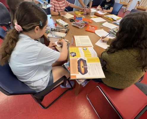 Des jeunes assis autour d'une table, entourés d'ouvrages de référence ouverts, de feuilles de papier colorées et de crayons